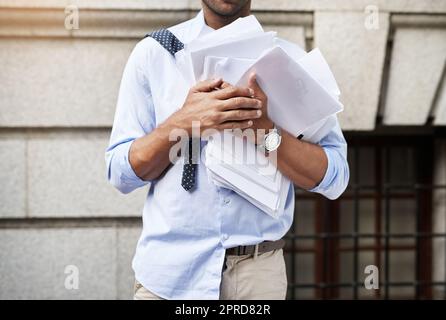 Ce sera une longue journée. Un jeune homme méconnaissable tenant un tas de documents en papier tout en marchant au travail le matin. Banque D'Images