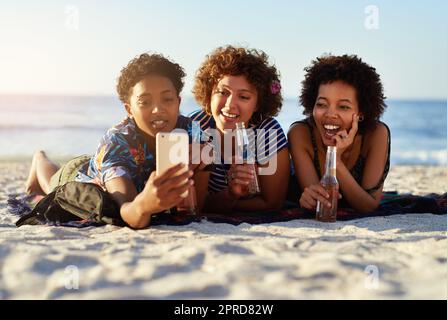 Souvenons-nous de ce moment à jamais. Un jeune trio de femmes s'asselas sur la plage et prenant des selfies ensemble pendant la journée. Banque D'Images