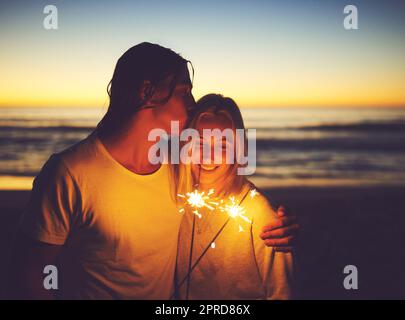 Chaque moment est rendu glorieux par la lumière de l'amour. Un jeune couple jouant avec des spameurs sur la plage la nuit. Banque D'Images