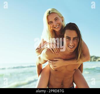 Nos jours sont toujours les plus brillants ensemble. Portrait d'un jeune homme donnant à sa petite amie une promenade en pigeyback à la plage. Banque D'Images