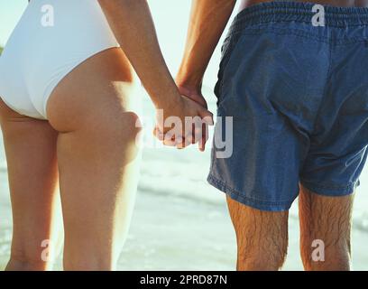 Summers le cadre parfait pour un peu de romantisme. Gros plan d'un couple tenant les mains à la plage. Banque D'Images