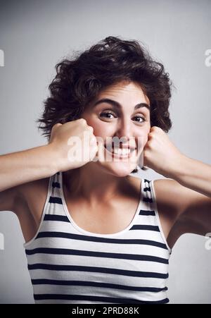 J'aime me pousser à Amuse-toi bien. Studio portrait d'une jeune femme attrayante faisant un visage drôle avec ses poings sur un fond gris. Banque D'Images