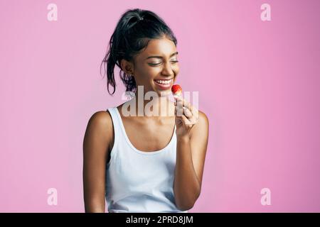 Shes appréciant cette fraise. Photo studio d'une belle jeune femme mangeant une fraise sur fond rose. Banque D'Images