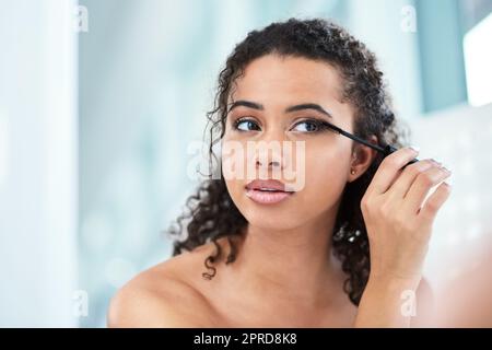 Plus les cils sont longs, mieux c'est une belle jeune femme qui applique la mascara dans son miroir de salle de bains. Banque D'Images