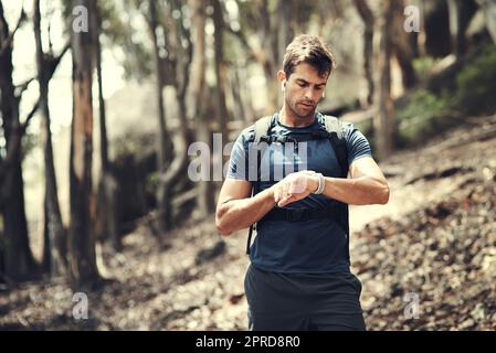 Comment suis-je faire pour le temps. Un beau jeune homme qui vérifie sa montre tout en randonnée dans les montagnes. Banque D'Images