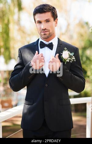 HES a l'air net et a l'air de se tacher le grand jour. Portrait d'un beau jeune marié qui ajuste son costume et se prépare à l'extérieur le jour de son mariage. Banque D'Images