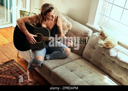 Certains des plus grands succès ont été réalisés à la maison. Une jeune femme jouant de la guitare lors d'une journée de détente à la maison. Banque D'Images