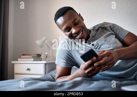 Répondant à mes messages texte. Un beau jeune homme allongé sur son lit et utilisant son téléphone portable alors qu'il est seul à la maison. Banque D'Images