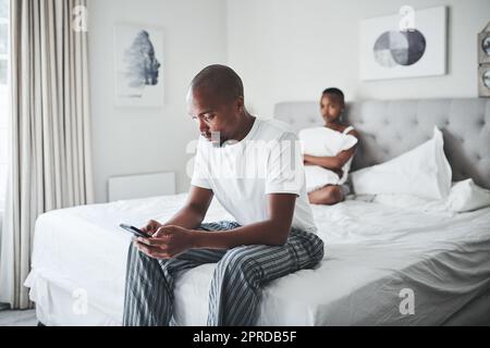 Il m'avait l'habitude de me tenir comme ça. Un jeune homme ignorant sa femme tout en utilisant un smartphone dans la chambre à la maison. Banque D'Images