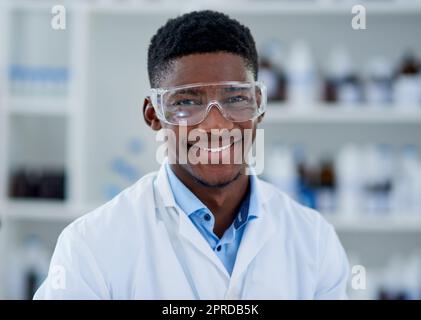 Comment puis-je regarder avec mes nouvelles lunettes. Portrait d'un jeune scientifique gai portant des lunettes de protection tout en se tenant à l'intérieur d'un laboratoire pendant la journée. Banque D'Images