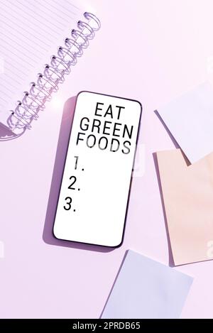 Légende de texte présentant Eat Green Foods. Mot écrit sur manger plus de légumes régime sain végétarien personne végétarienne téléphone mobile avec message important sur le bureau avec un carnet et des notes vides. Banque D'Images