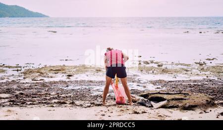 Ne laissez rien sur la plage, mais vos empreintes. Vue arrière d'un homme ramassant la litière dans une plage polluée et sale à Raja Ampat, Indonésie. Banque D'Images