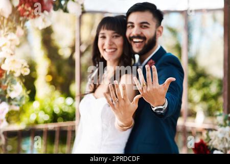 Nous venons de devenir M. et Mme un jeune couple affectueux et jeune jeune jeune couple qui a fait clignoter leurs anneaux de mariage tout en étant debout à l'extérieur le jour de leur mariage. Banque D'Images