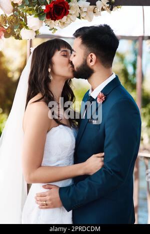 Un baiser est une autre façon de communiquer l'amour avec vos lèvres. Un jeune couple affectueux et jeune, qui embrasse tout en se tenant debout à l'extérieur le jour de leur mariage. Banque D'Images