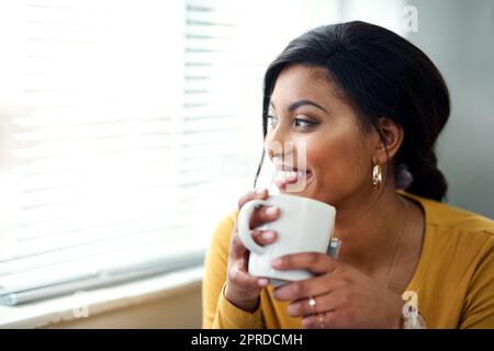 J'aime mes matins. Une jeune femme attrayante assise seule et buvant une tasse de thé dans sa maison. Banque D'Images