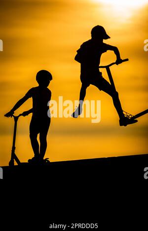 Silhouette d'un jeune garçon à bord d'un scooter sur fond de coucher de soleil Banque D'Images