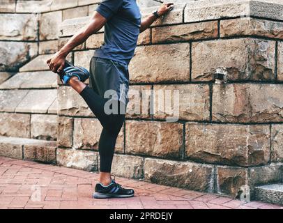 N'oubliez jamais de vous étirer avant de commencer un exercice. Un sportif méconnaissable s'étirant et se réchauffant avant de faire de l'exercice à l'extérieur dans la ville. Banque D'Images