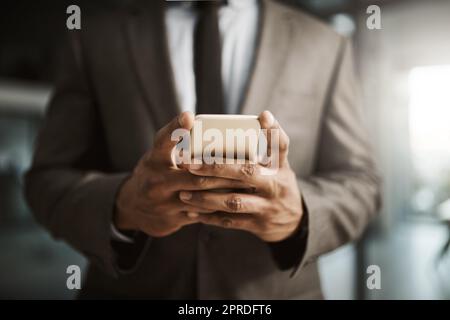 Un homme d'affaires envoie un SMS sur un téléphone pour envoyer un SMS professionnel formel à l'intérieur d'un bureau au travail. Un homme de direction d'entreprise africain portant un costume tapant un e-mail à son client en ligne gros plan Banque D'Images