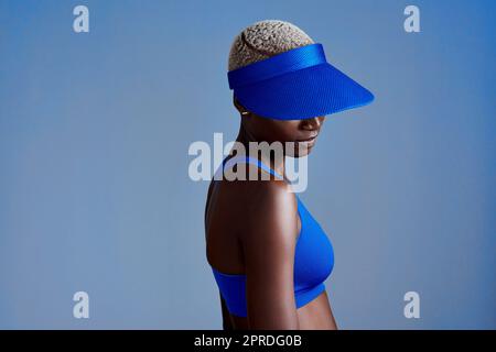 Votre visière est votre protection. Photo en studio d'une jeune femme sportive portant une visière tout en posant sur un fond bleu. Banque D'Images