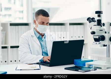 Le temps est compté pour trouver un remède. Un jeune scientifique utilisant un ordinateur portable tout en travaillant sur un traitement du coronavirus dans un laboratoire. Banque D'Images