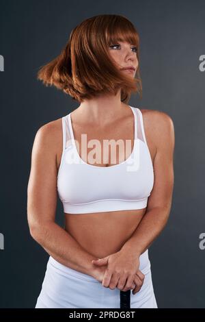 Jouer au sport est ce qui me permet de continuer. Photo en studio d'une jeune femme attrayante posant avec un bâton de hockey sur fond gris. Banque D'Images