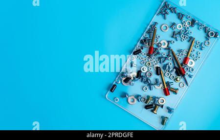 Vue de dessus boulons métalliques, écrous, rondelle et vis dans un plateau en plastique sur fond bleu. Matériel de fixation. Outils matériels des techniciens en mécanique. Accessoires de fixation filetés. Vis et écrous de fixation Banque D'Images