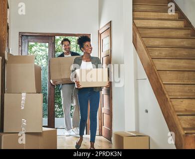 Couple interracial se déplaçant dans une nouvelle maison moderne, transportant des boîtes et arrivant à la maison ensemble. Un mari et une femme heureux, excités et souriants qui marchent, entrent et déménagent après avoir acheté un appartement Banque D'Images