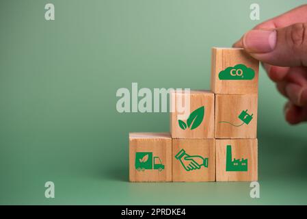 Main tenant en bois cube bloc icône CO2 carbone crédit et écoénergie technologie verte sur fond vert. Banque D'Images