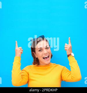 Veillez à laisser vos commentaires dans la section ci-dessus. Portrait court d'une jeune femme heureuse pointant vers le haut sur fond bleu. Banque D'Images