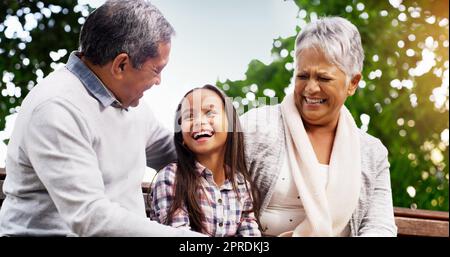 Nous avons toujours les meilleurs moments ensemble. Une petite fille gaie assise sur un banc avec ses grands-parents au parc. Banque D'Images