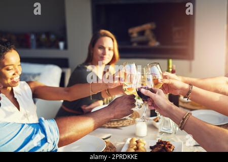 Un groupe d'amis qui élèvent leurs lunettes pour un toast tout en étant assis autour d'une table à l'extérieur. Banque D'Images