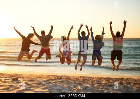 Sautez et laissez la mer vous libérer. Vue arrière d'un groupe de jeunes amis qui sautent dans les airs à la plage. Banque D'Images