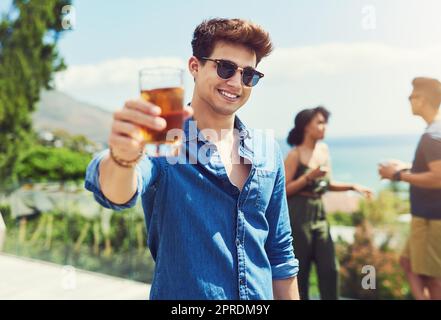 J'espère que tout le monde profite aussi de leurs vacances. Portrait d'un beau jeune homme qui lève son verre pour un toast tout en se relaxant dehors avec ses amis. Banque D'Images