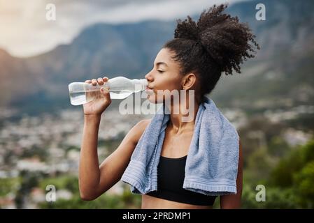 L'eau purifie le corps et l'âme. Une jeune femme sportive boit de l'eau tout en faisant de l'exercice à l'extérieur. Banque D'Images