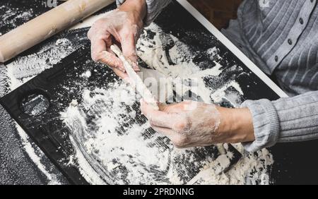 deux mains de femmes pétrient la pâte de farine de blé blanc sur une table noire, vue de dessus Banque D'Images