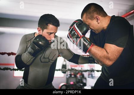 Absorbez les coups. Deux boxeurs de sexe masculin se font face l'un à l'autre dans un match d'entraînement à l'intérieur d'un anneau de boxe dans une salle de gym pendant la journée. Banque D'Images