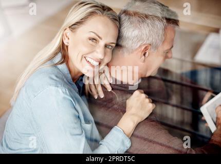 Passer ma vie avec lui a été la meilleure décision jamais prise. Une femme mûre embrassant son mari alors qu'il utilise une tablette numérique sur le canapé à la maison. Banque D'Images