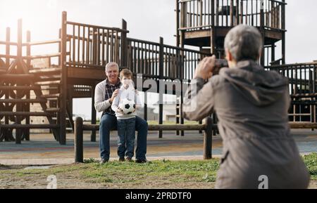 Étaient si fiers de lui. Vue arrière d'une grand-mère prenant une photo de son mari et de son petit-fils se posant ensemble à l'extérieur. Banque D'Images