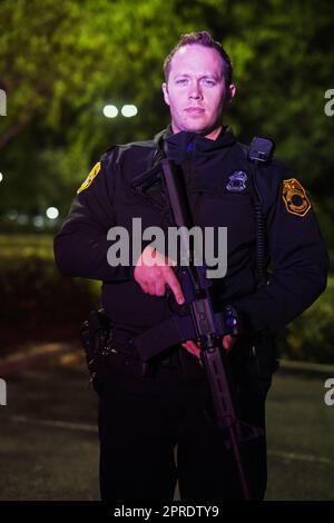 Ce travail n'est pas pour tout le monde. Portrait court d'un beau jeune policier debout avec son fusil d'assaut pendant sa patrouille. Banque D'Images