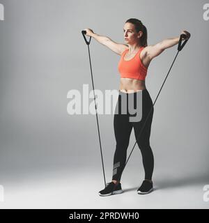 La formation de résistance est bonne pour tout le corps. Photo en studio d'une jeune femme sportive qui s'efforce avec un bracelet de résistance sur fond gris. Banque D'Images