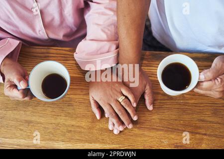 Nous jouissons des choses simples dans la vie. Gros plan en grand angle d'un couple méconnaissable qui tient les mains tout en buvant du café sur une table à la maison pendant la journée. Banque D'Images