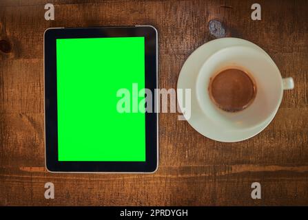 Café et wifi Oui s'il vous plaît. Photo en grand angle d'une tablette numérique avec écran vert et une tasse de café sur une table. Banque D'Images