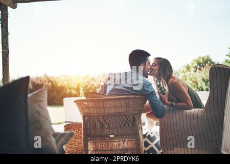 Les meilleurs sièges de la maison. Photo d'un jeune couple affectueux qui embrasse tout en dégustant des bières sur leur patio. Banque D'Images