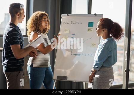 En arrondissant les dernières statistiques, un groupe de jeunes designers remue un tableau blanc dans un bureau. Banque D'Images