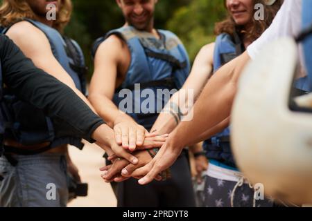 Ici pour radeau, ici pour rire, faisons ceci. Un groupe de jeunes amis masculins se joignant à la main dans l'unité avant de faire du rafting en eau vive. Banque D'Images