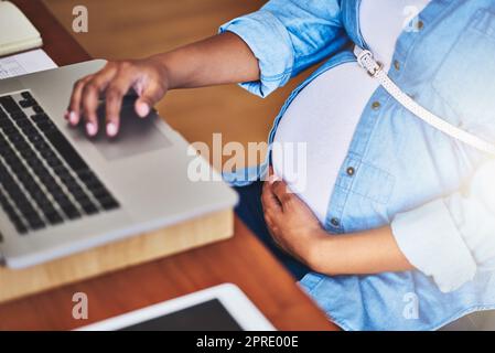 Faire les choses avec bébé à bord. Une femme enceinte utilisant un ordinateur portable tout en travaillant de la maison. Banque D'Images