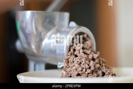 Hachez la viande hachée dans un moulin à viande mécanique manuel. La viande fraîche bouillie est hachée avec un vieux moulin à viande en métal, en gros plan dans la cuisine. Banque D'Images