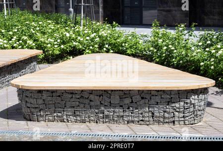 Bancs en bois de paniers de gabion avec pierres à l'intérieur. Bois monté sur gabions. Bancs de design moderne. Détail d'un mur de gabion bas recouvert de bois pour une utilisation comme banc. Banque D'Images