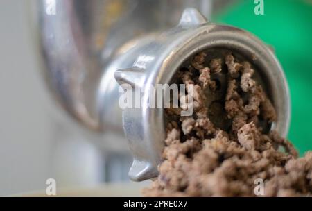 Hachez la viande hachée dans un moulin à viande mécanique manuel. La viande fraîche bouillie est hachée avec un vieux moulin à viande en métal, en gros plan dans la cuisine. Banque D'Images