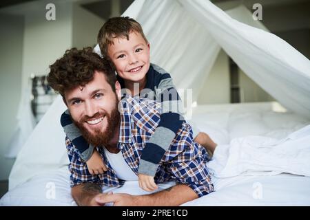 HES m'a toujours pris le dos. Portrait court d'un beau jeune homme allongé sur le lit à la maison avec son fils sur le dos. Banque D'Images